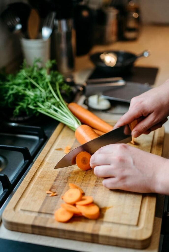 Top-down view of hands using kitchen knives to prep veggies, bread, fruit, herbs, cheese, and fish.